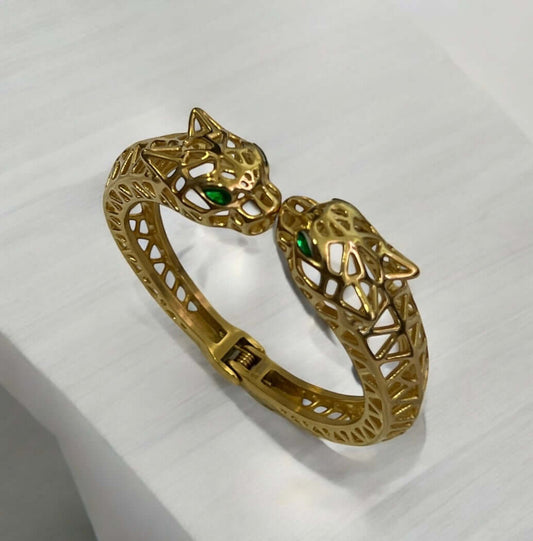 Gold bracelet with two panther heads featuring green gemstones, showcasing elegant design and craftsmanship.